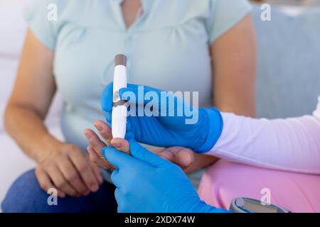Infermiera in guanti blu che controllano il livello di zucchero nel sangue della donna anziana a casa Foto Stock