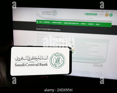 Persona che detiene lo smartphone con il logo dell'istituto finanziario Saudi Central Bank (SAMA) davanti al sito web. Mettere a fuoco il display del telefono. Foto Stock