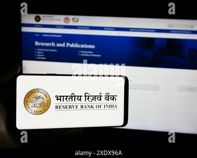 Persona che detiene un telefono cellulare con il logo della banca centrale indiana Reserve Bank of India (RBI) di fronte alla pagina web. Mettere a fuoco il display del telefono. Foto Stock