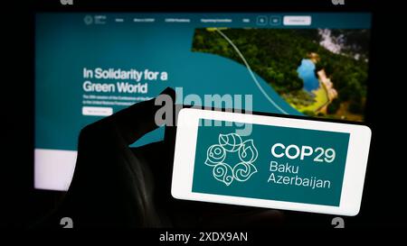 Persona che possiede uno smartphone con il logo della Conferenza delle Nazioni Unite sui cambiamenti climatici 2024 COP29 davanti al sito web. Mettere a fuoco il display del telefono. Foto Stock