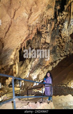 Una donna sta di fronte a un muro di una grotta, guardando in alto le formazioni rocciose della grotta. La grotta è buia e umida, con un senso di mistero e meraviglia. Foto Stock
