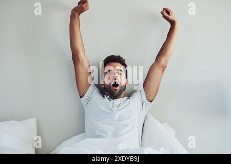 Svegliati, sbadiglio e stanco che si allunga nel letto per ustioni, stanchezza o recupero a casa sullo sfondo della parete. Pace, mattina o persona pigra in camera da letto Foto Stock