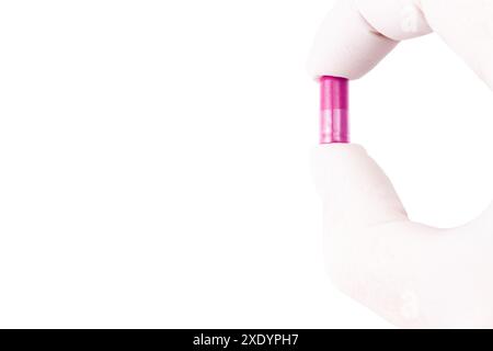 Mano in guanto medico che tiene la capsula di plastica di colore rosa organico med isolato su sfondo bianco primo piano Foto Stock