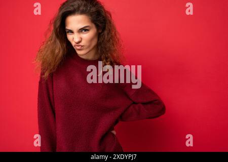 Giovane, bella donna bruna riccia e arrabbiata, con emozioni sincere che si riversano isolata sulla parete di fondo con spazio di copia che indossa cas Foto Stock
