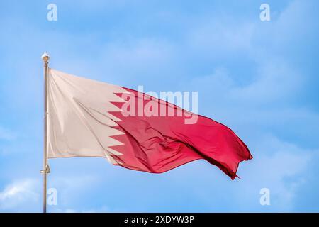 La bandiera nazionale del Qatar sta volando nel vento contro il cielo blu. Primo piano Foto Stock