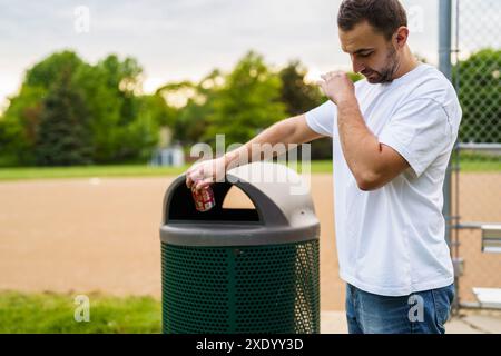 Un giovane che getta la spazzatura in un bidone all'aperto. Riciclaggio. Foto Stock