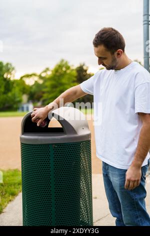 Uomo che cammina con rifiuti. Portare a mano il sacchetto di plastica contro i bidoni della spazzatura sulla strada. Foto Stock
