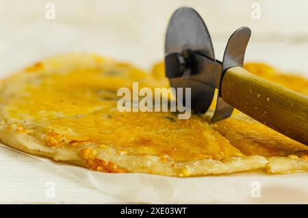 Primo piano. Tagliare la pizza appena sfornata con un tagliapasta. Foto Stock