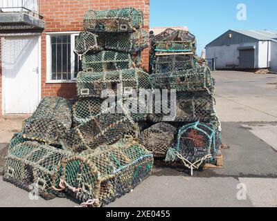 Pentole di aragosta utilizzate nella pesca tradizionale per i crostacei impilati contro un edificio sul porto di scarborough Foto Stock