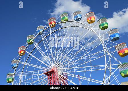 Colorate gondole della ruota panoramica, gialle, verde, blu e rosso contro un cielo blu e una nuvola bianca in una giornata di sole al Luna Park di Sydney Foto Stock