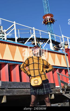 Una giornata di cielo azzurro al Luna Park sul porto di Sydney, una donna felice con i colori del carnevale e giostre del parco divertimenti, The Hair Raiser & Wild mouse Foto Stock