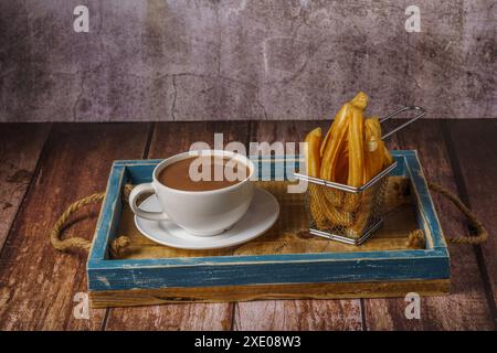 Cioccolata calda in una tazza bianca con churros in un vassoio di legno blu Foto Stock