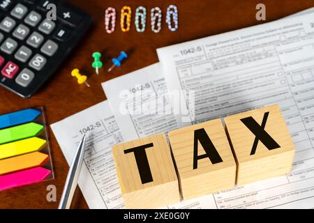 Un blocco di legno con la parola "tax". Il blocco è sopra una pila di carte e una calcolatrice. Pagare l'aliquota fiscale. Tasse, oneri fiscali. Foto Stock