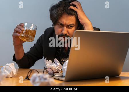 Giovane uomo d'affari che beve dallo stress. Dipendenza da alcol, uomo d'affari ubriaco con un bicchiere di whisky Foto Stock
