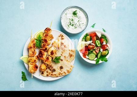 Kebab di pollo souvlaki, insalata greca di verdure e focaccia pita blu, vista dall'alto. Pasto sano mediterraneo - spiedini di carne e insalata, tzadziki sau Foto Stock