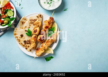 Kebab souvlaki di pollo, insalata greca di verdure e focaccia pita su sfondo blu, vista dall'alto, spazio per copiare. Pasto sano mediterraneo - spiedini di carne Foto Stock