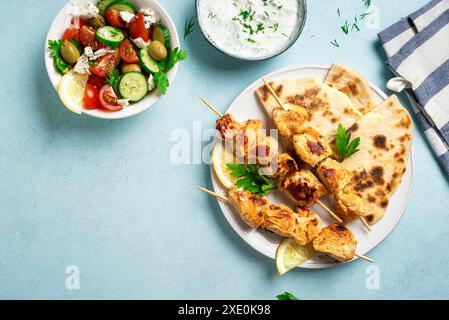 Kebab souvlaki di pollo, insalata greca di verdure e focaccia pita su sfondo blu, vista dall'alto, spazio per copiare. Pasto sano mediterraneo - spiedini di carne Foto Stock