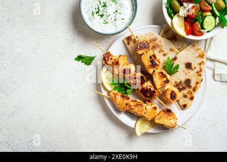 Pranzo salutare mediterraneo: Spiedini di pollo souvlaki, focaccia e insalata di verdure. Kebab di pollo fritto, insalata greca, salsa di yogurt tzatziki e pi Foto Stock