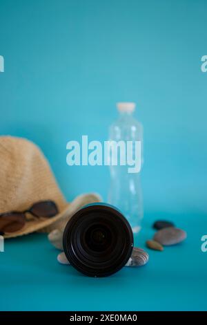 lente, cappello di paglia, occhiali da sole, bottiglia d'acqua, spray per crema solare, ciottoli su sfondo colorato Foto Stock