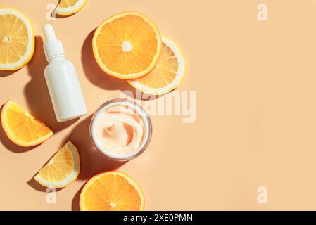 Siero di vitamina C naturale e crema viso, dermocosmesi, prodotti a base di olio essenziale. Prodotti cosmetici e frutta fresca e succosa al limone e all'arancia fettina su bac arancio Foto Stock