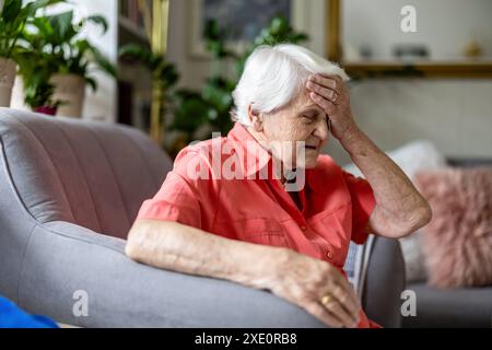 Donna anziana seduta su una poltrona che soffre di mal di testa Foto Stock