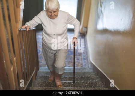 Donna anziana che sale le scale appoggiata su un bastone di legno Foto Stock