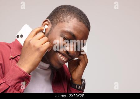 primo piano di un giovane afroamericano che ascolta la musica tramite cuffie wireless e si sente rilassato e felice Foto Stock