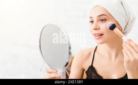 Donna che applica il trucco in una Bright Room durante la routine mattutina Foto Stock