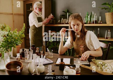 Profumiera femminile seduta a tavola e tester odorante mentre il profumiere maschio maturo legge note Foto Stock