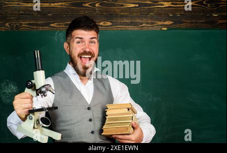 Lezione di chimica o biologia. Insegnante o studente felice con libri e microscopio in classe vicino alla lavagna. Lavoro pratico in chimica. Ricerca Foto Stock