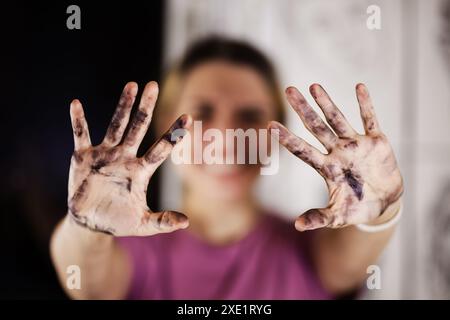 Una pittrice con una camicia viola casual mostra le sue mani disordinate, ricoperte di vernice, a simboleggiare la creatività e l'espressione artistica. Foto Stock