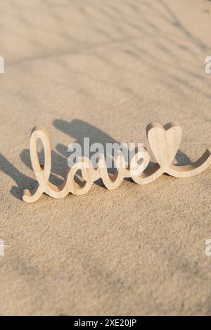 Parola amore in legno su sfondo spiaggia sabbiosa. Concetto di anniversario romantico delle vacanze, proposta, biglietto d'auguri per il giorno delle valentine, pos Foto Stock