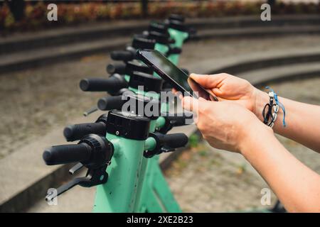 La mano femminile utilizza il telefono cellulare per scansionare il codice QR sullo scooter elettrico per strada sull'app di servizio e-scooter. tr. Alternativo Foto Stock