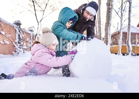 Una famiglia costruisce un pupazzo di neve bianca nel cortile in inverno. Foto Stock