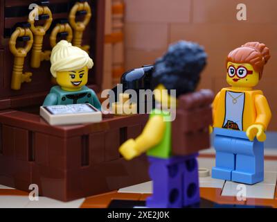 Tambov, Federazione Russa - 21 giugno 2024, Una minifigura della receptionist Lego in piedi dietro il tavolo del ricevimento in un hotel e che parla con gli ospiti dell'hotel Foto Stock