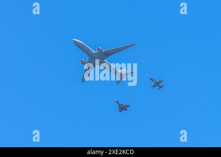Gijon, Spagna - 24 maggio 2024: Un grande aereo cargo vola in alto nel cielo, accompagnato da due caccia più piccoli. Sagome di aerei si infilano contro di loro Foto Stock