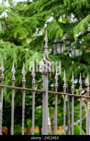 Palo per recinzione in ferro dal design complesso con motivo decorativo ritorto con una cima appuntita circondata da vegetazione verde del parco Foto Stock