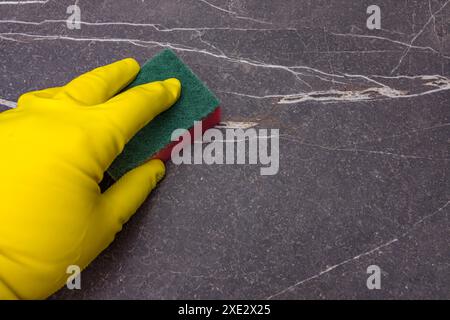 La mano maschio in guanto di gomma pulisce una superficie di marmo scuro con un tampone abrasivo Foto Stock