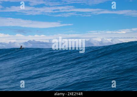 Teahupoo, Tahiti, Polinesia francese - 7 giugno 2024 un surfista solitario che rema su un'onda mostruosa. Teahupoo è la sede dell'evento olimpico di surf 2024. Foto Stock