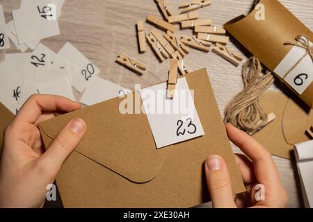 La giovane donna irriconoscibile attacca il numero sulla borsa artigianale, si aggancia con un clothespin. Donna che produce carta kraft per l'avvento fatto in casa ca Foto Stock