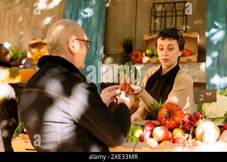 Piccola impresa gestita da donna che vende frutta e verdura biologica presso uno stand del mercato agricolo locale. Il fornitore del mercato alimentare mostra a un cliente senior prodotti freschi e sostenibili in un negozio di agricoltura all'aperto. Foto Stock