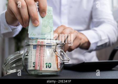 Euro Banknote risparmio in vaso di vetro. Uomo irriconoscibile consumo moderato su calcolatrice e economia raccogliere denaro Consigli Foto Stock