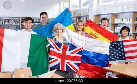 Ritratto di adolescenti positivi e insegnante femminile con bandiere di diversi paesi nella biblioteca scolastica Foto Stock