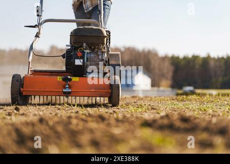 Uomo che usa una macchina aeratrice per la scarificazione e l'aerazione di prati o prati Foto Stock