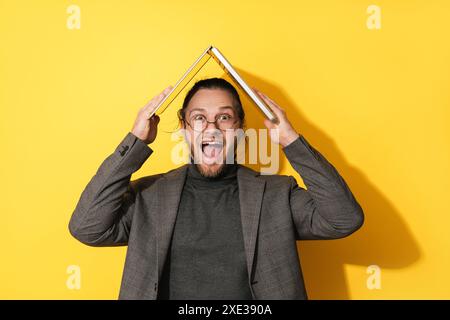 Allegro uomo barbuto che tiene il computer portatile sopra la testa su sfondo giallo Foto Stock