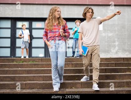 Gli studenti escono dalle porte dell'università. Il ragazzo punta la mano a qualcuno Foto Stock