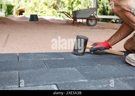 Mani di un lavoratore che posa pavimentazione, grandi blocchi di asfaltatrice per calcestruzzo con martello in mano. Posa di calcestruzzo pav Foto Stock