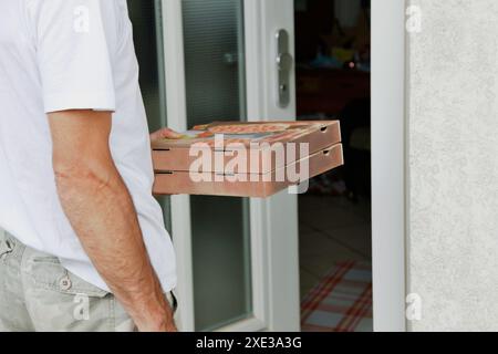 Due scatole per pizza in mano a un uomo in piedi sulla porta. Consegna pizza, corriere. Lavoratore di consegna di cibo se Foto Stock