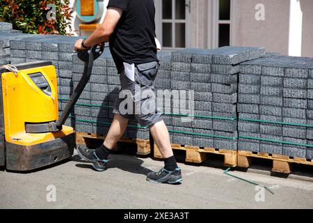 Un sollevatore con transpallet a forche con una pila di lastre di pavimentazione in calcestruzzo. addetto alle consegne con martinetto per pallet, Foto Stock