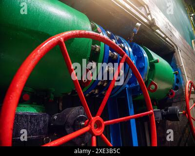 Primo piano di valvole e tubazioni industriali. Vista dettagliata dei macchinari verdi e blu con ruota della valvola rossa prominente, essenziale per il controllo del flusso nelle impostazioni di fabbrica. Foto Stock